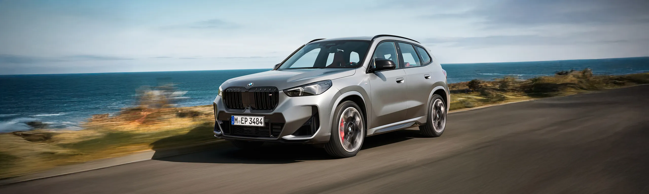 BMW X5 blanco circulando por carretera costera con vistas al mar