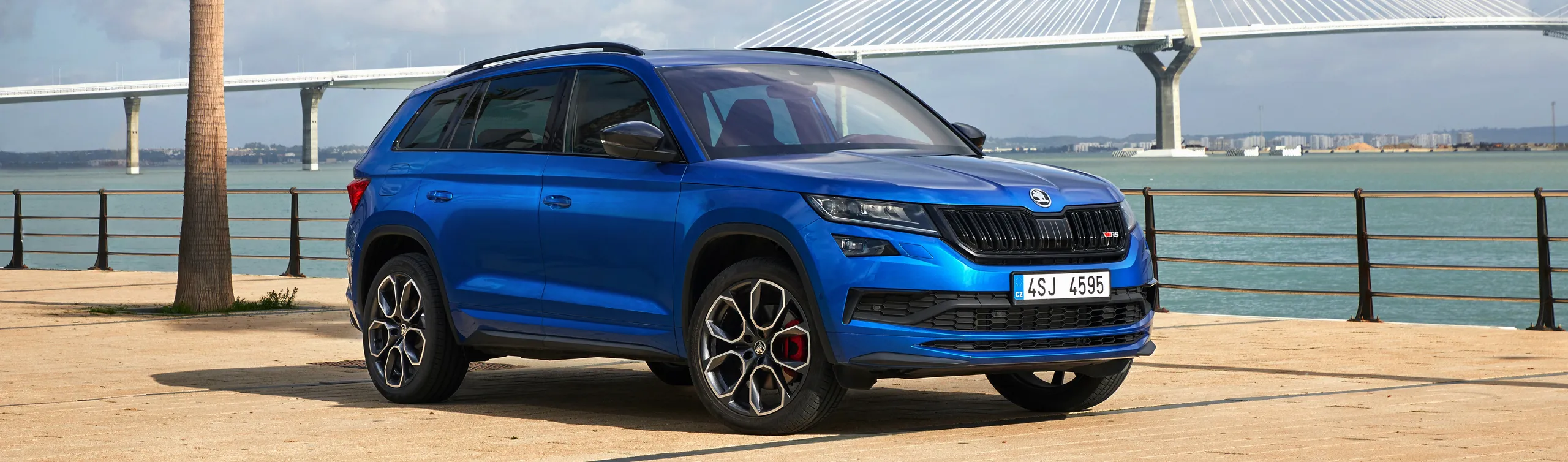 Skoda Kodiaq azul aparcado en paseo marítimo con puente al fondo
