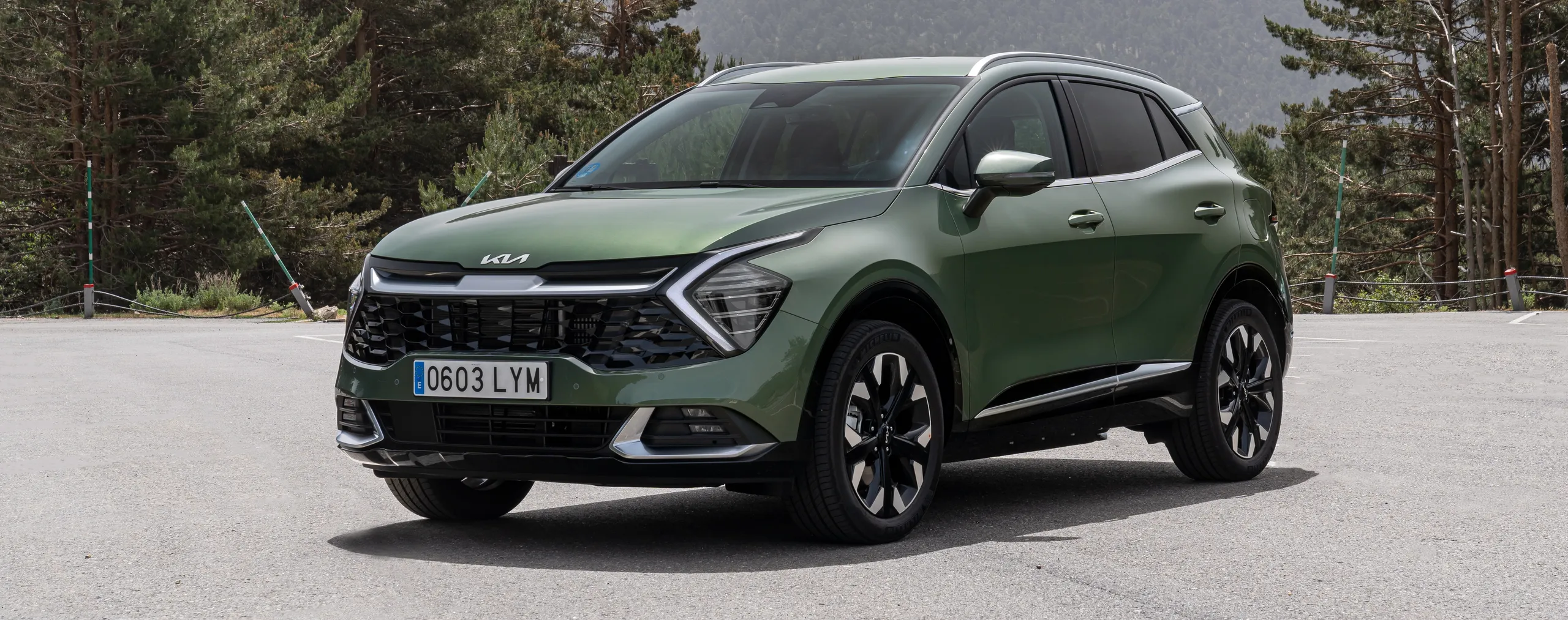 Kia Sportage verde oscuro en posición lateral en carretera de montaña