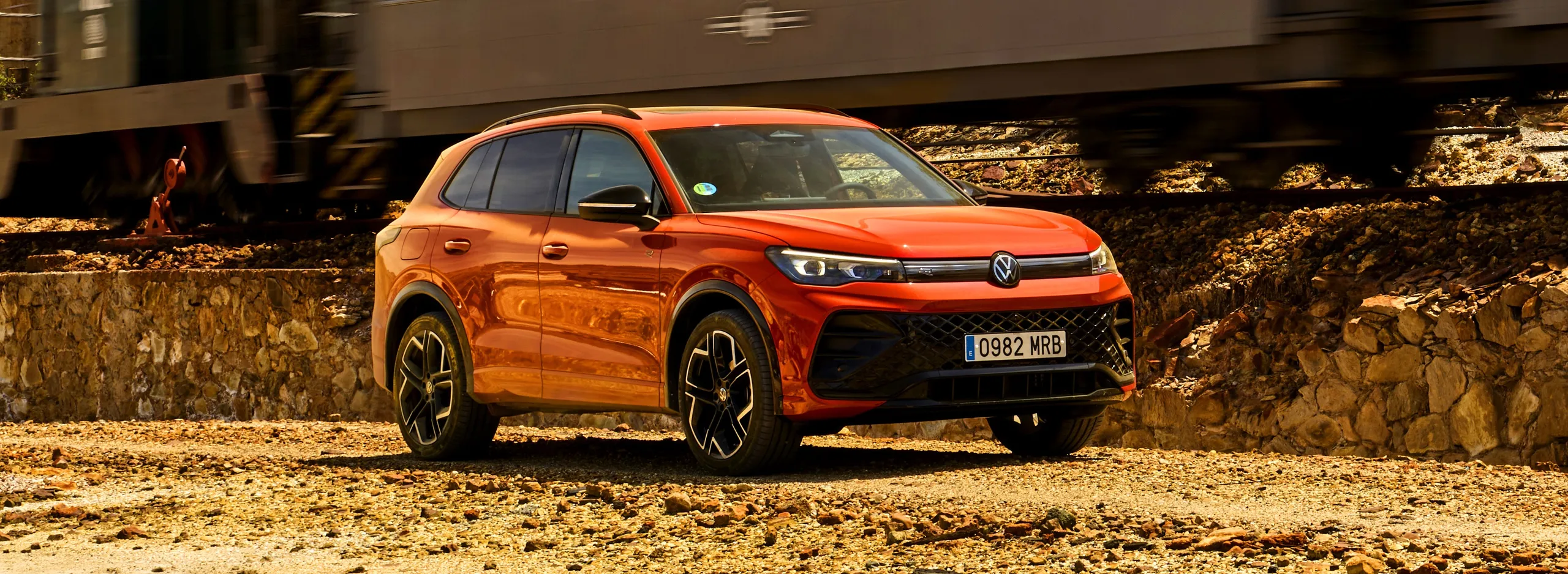 Volkswagen Tiguan naranja aparcado en zona de tierra con muros de piedra