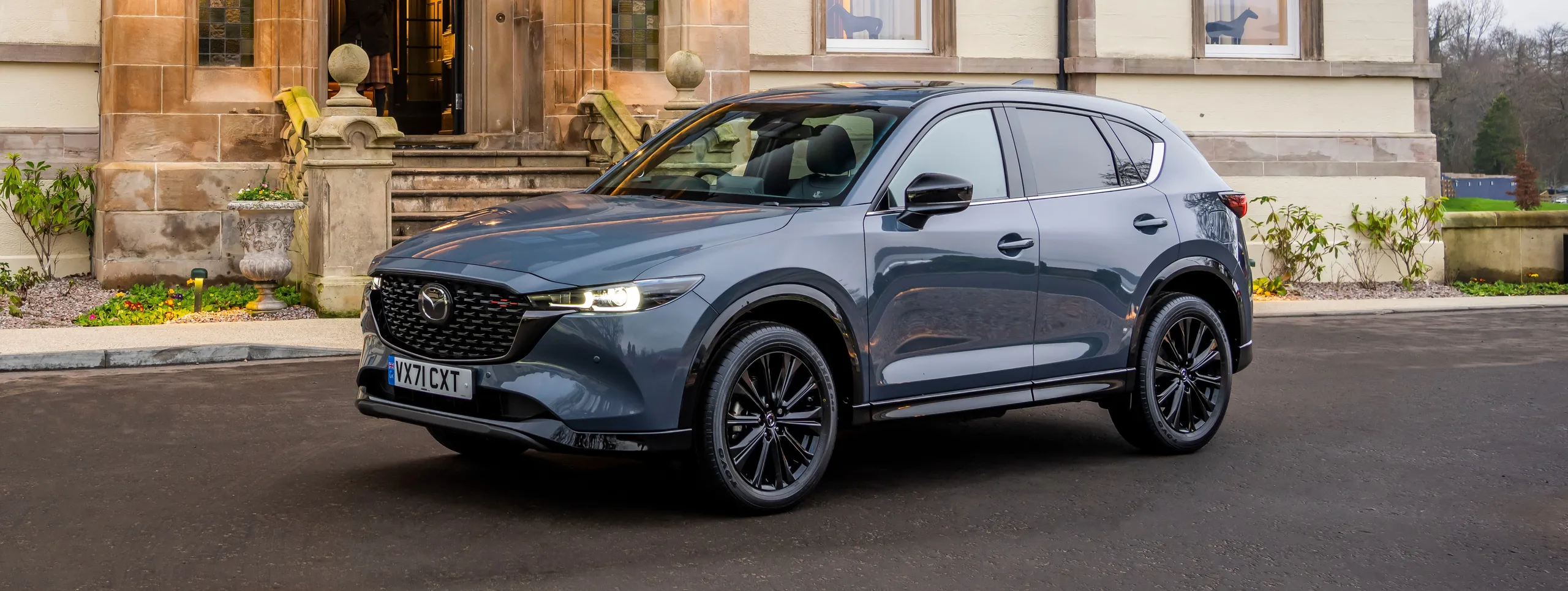 Mazda CX-5 azul oscuro de perfil junto a edificio de piedra arenisca