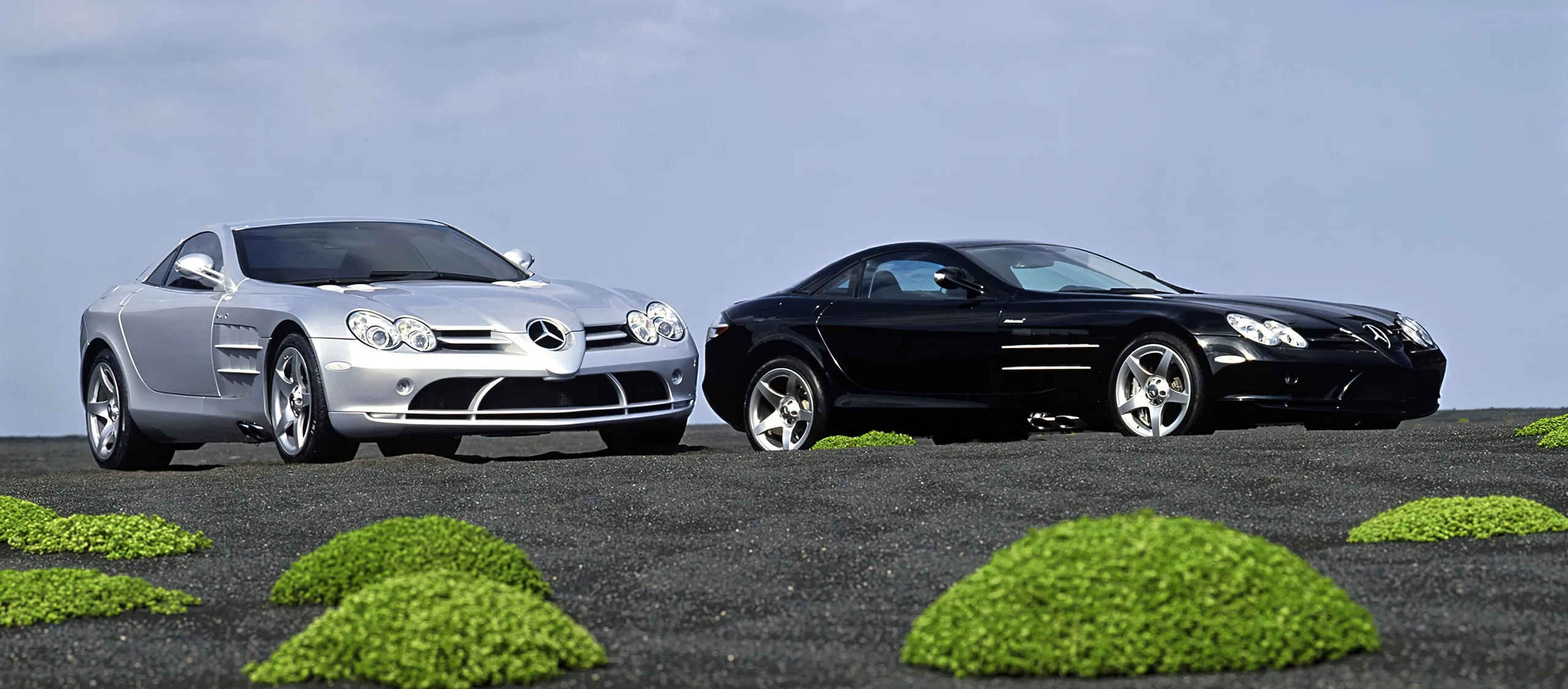 Dos Mercedes SLS AMG, uno plateado y otro negro, con puertas abiertas verticales