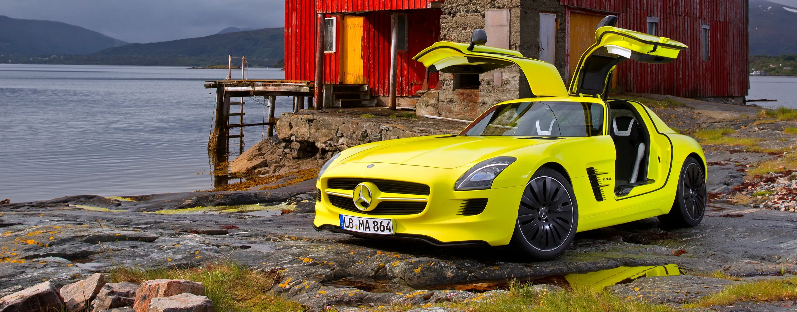 Mercedes-Benz SLS AMG amarillo neón con puertas abiertas en paisaje costero