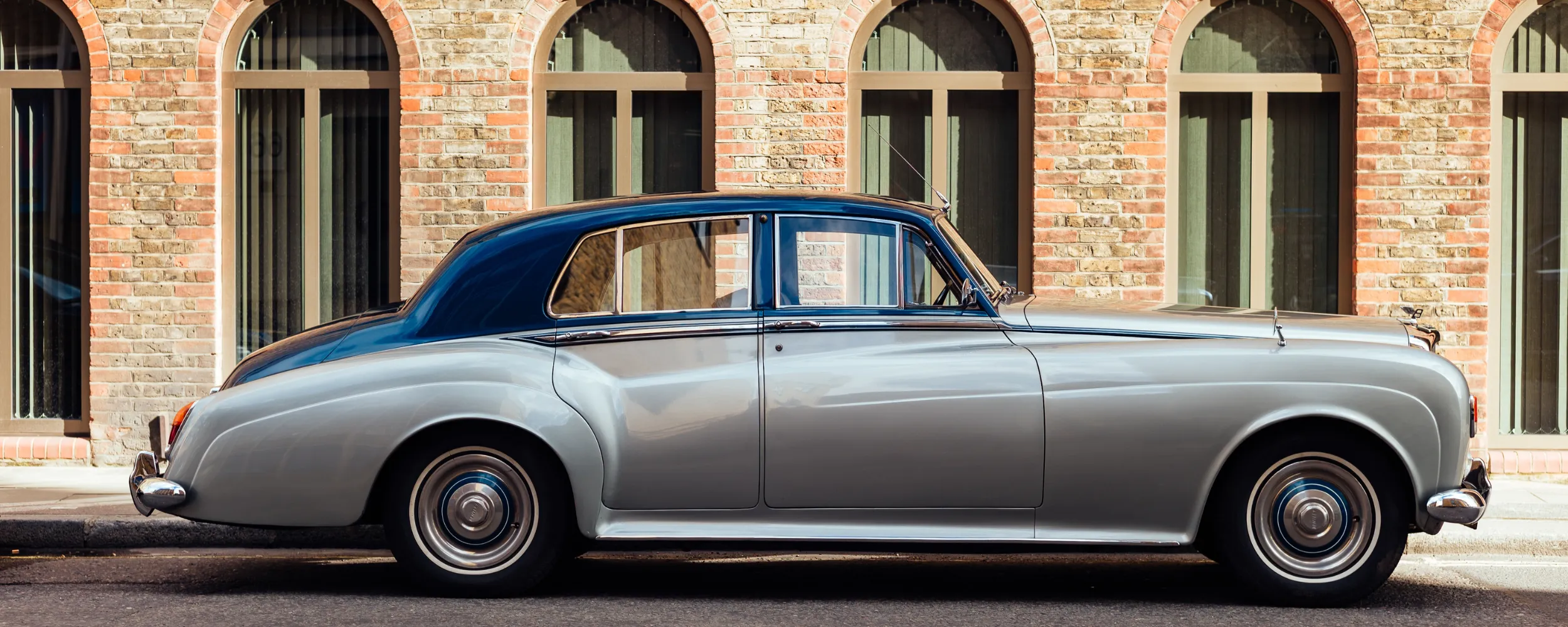 Coche clásico de lujo años 50 con distintivo H aparcado frente a edificio histórico