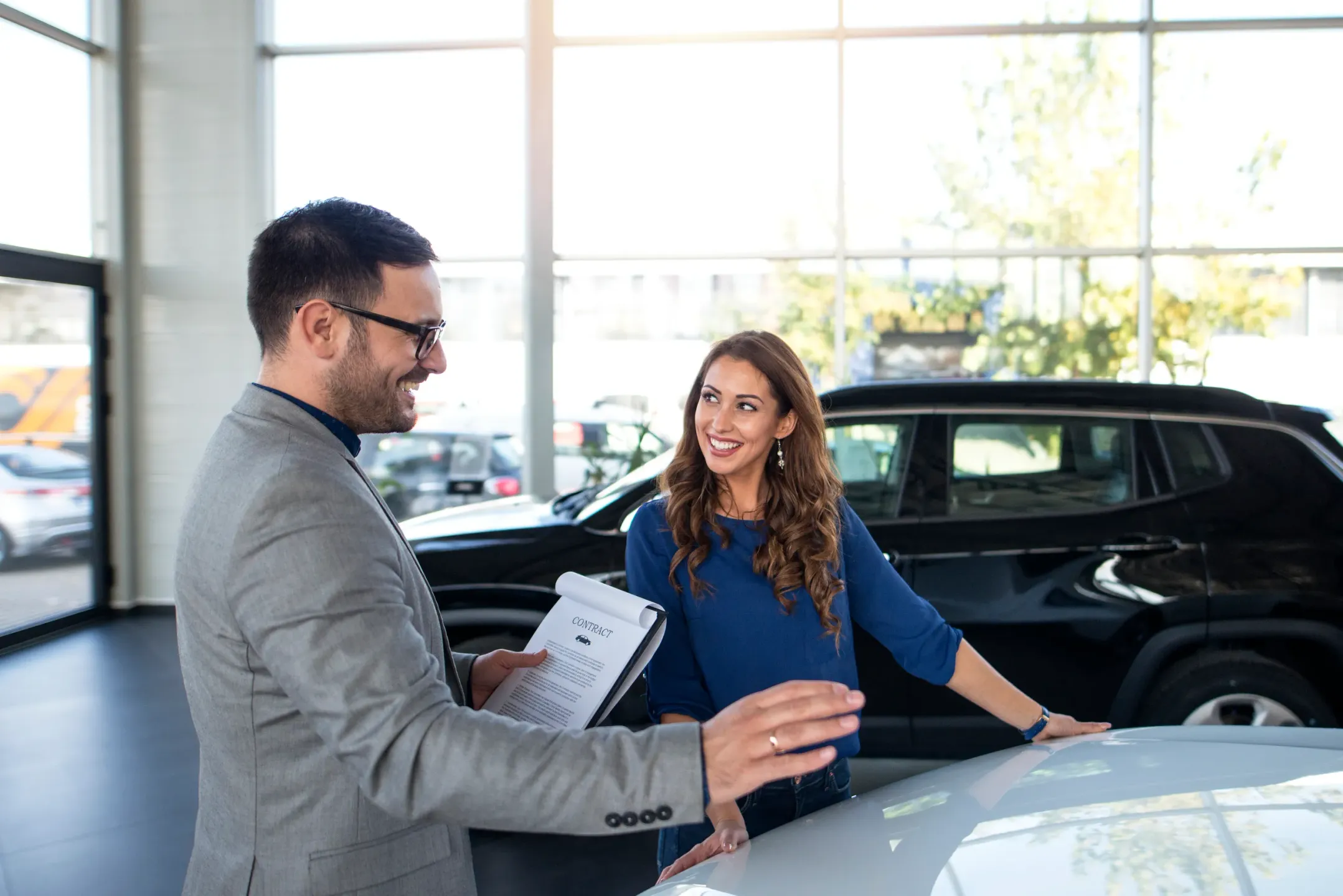 Vendedor mostrando contrato de venta a cliente en concesionario de coches