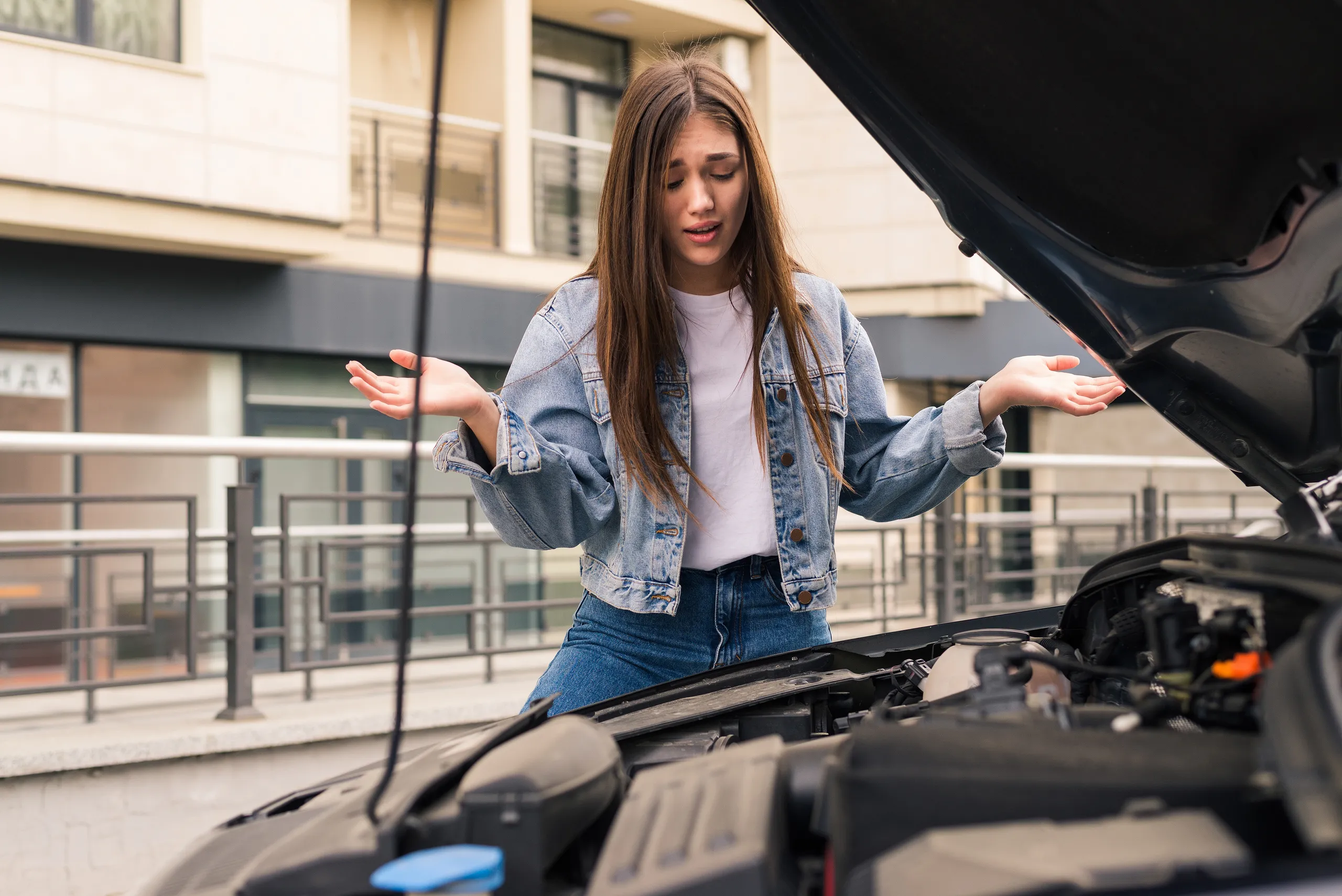 Mujer revisando el motor de un coche con capó abierto en la calle