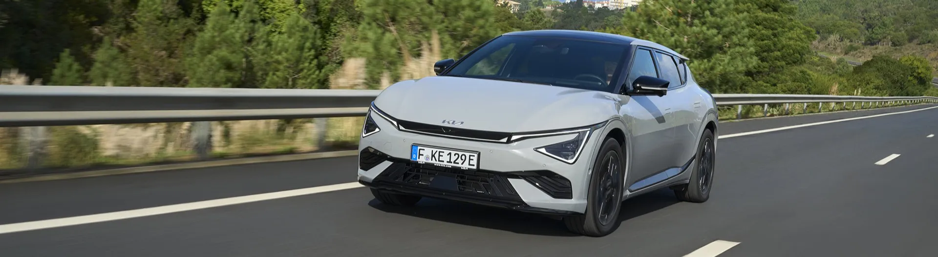 Kia EV6 blanco circulando por autopista entre bosques, ejemplo de coche eléctrico moderno