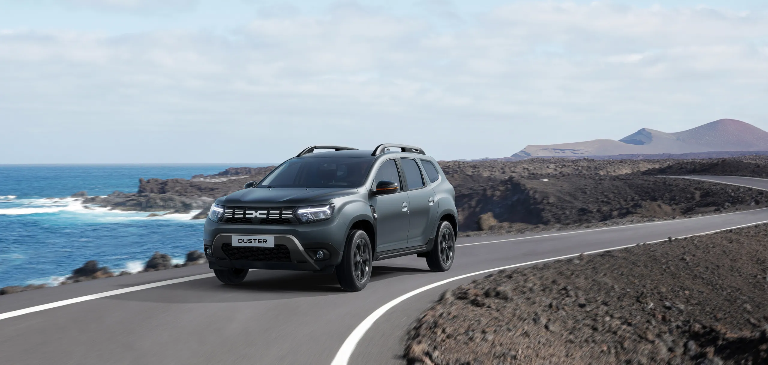 Dacia Duster gris circulando por carretera costera con paisaje volcánico