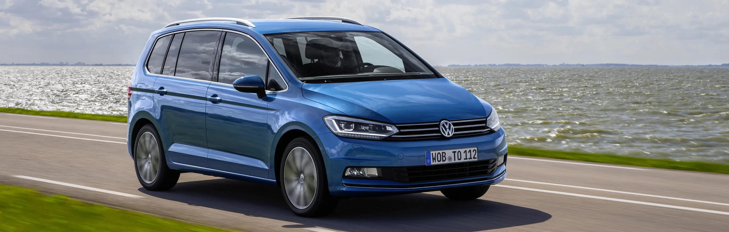 Volkswagen Touran azul circulando por carretera junto al mar