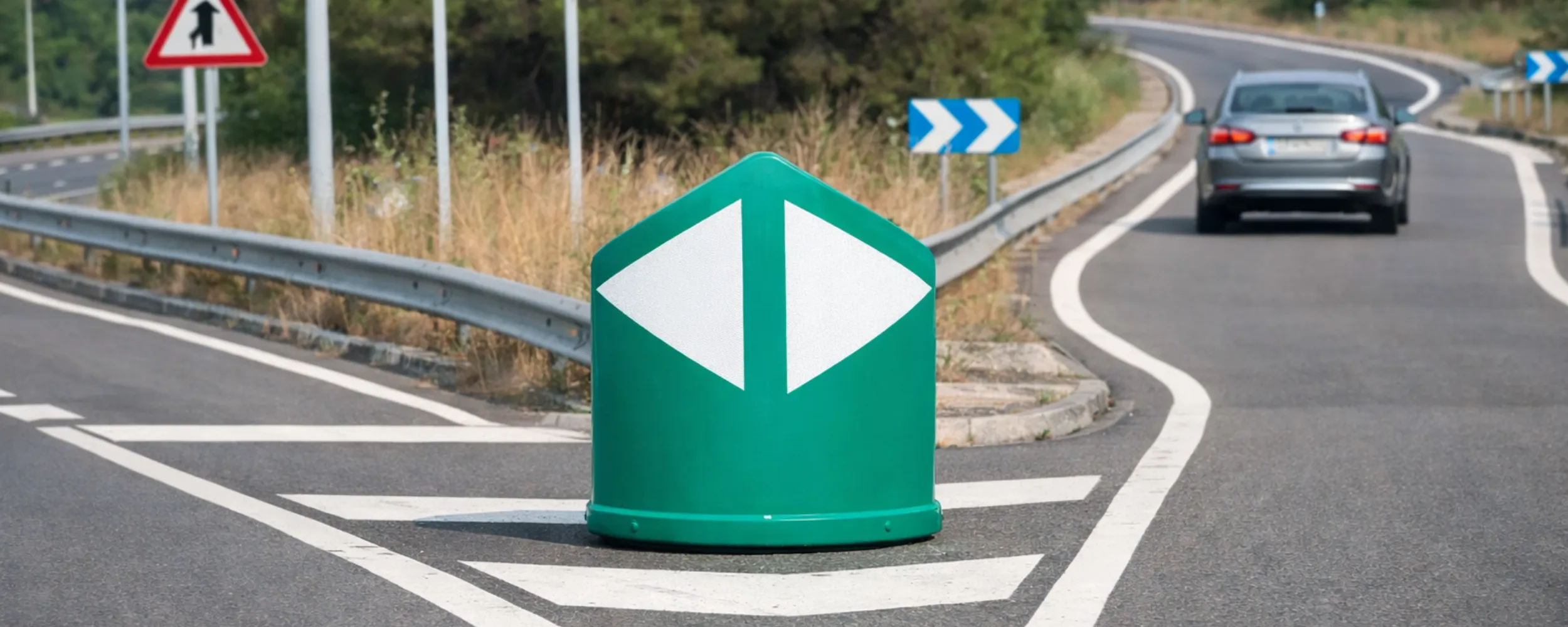 Panel de balizamiento verde en curva de autopista con vehículos