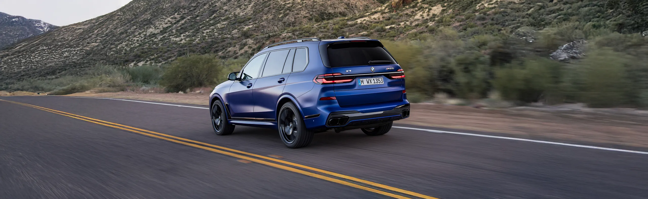 BMW X5 azul circulando por carretera de montaña con amplio maletero
