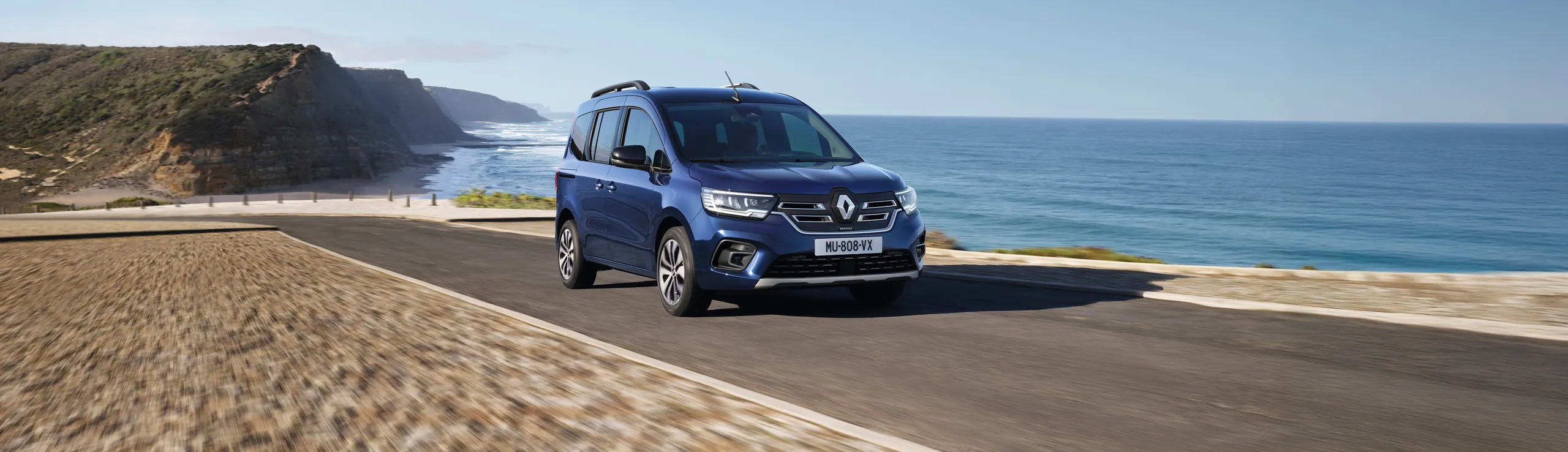 Renault Kangoo azul circulando por carretera costera con vistas al mar