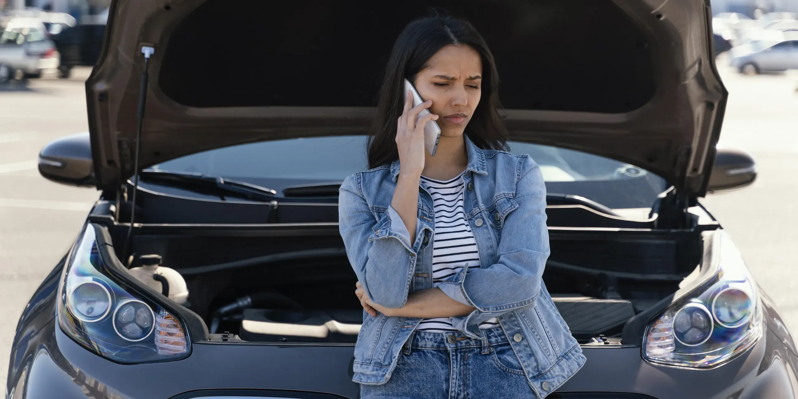 Mujer llamando por teléfono junto a coche con capó abierto en taller