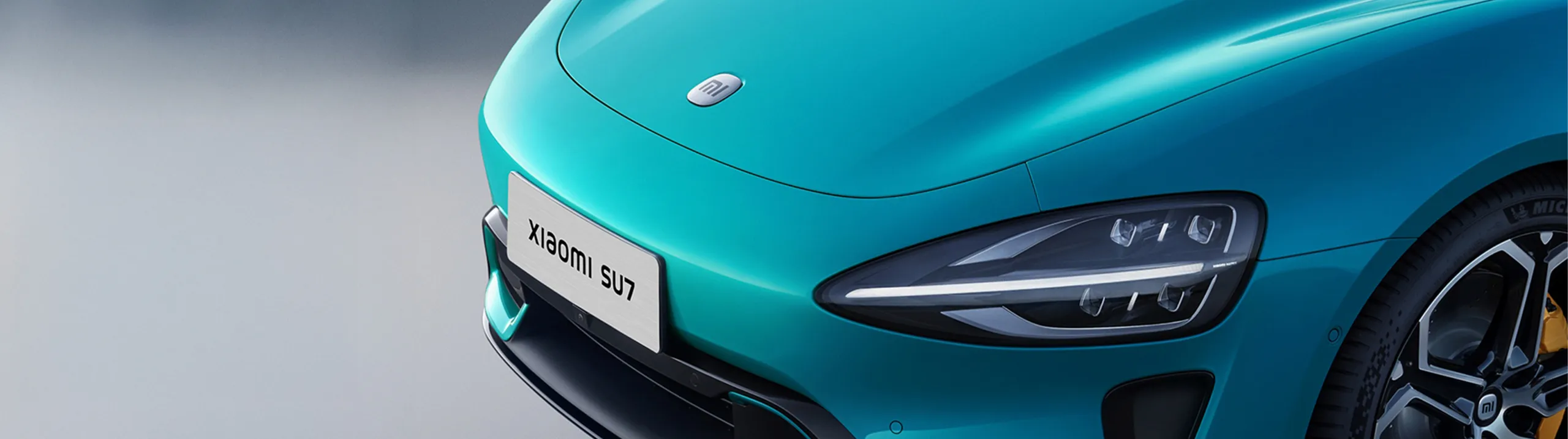 Detalle frontal del Xiaomi SU7 turquesa con faros LED y placa identificativa