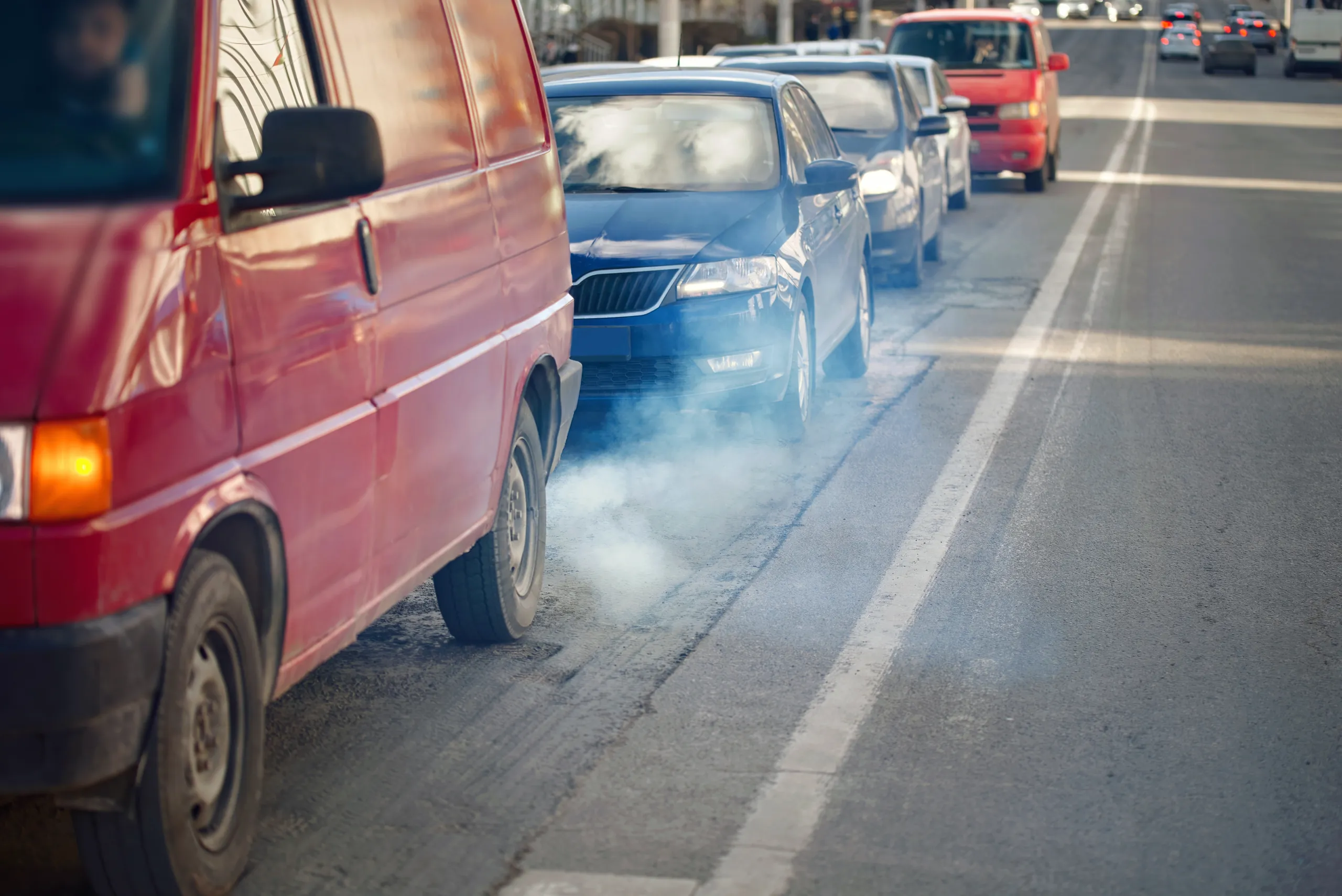 Tráfico congestionado con vehículos emitiendo humo de escape en una avenida